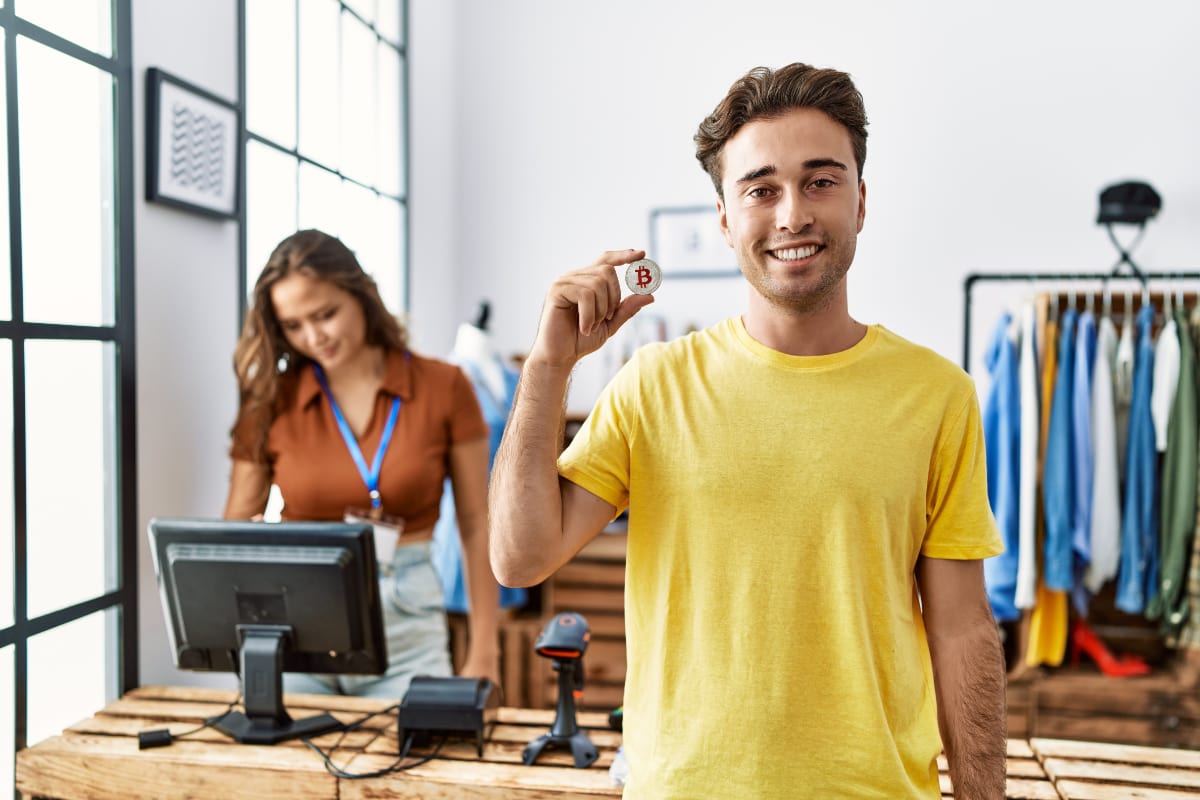 Should you accept cryptocurrencies in your business? young man showing bitcoin in retail shop