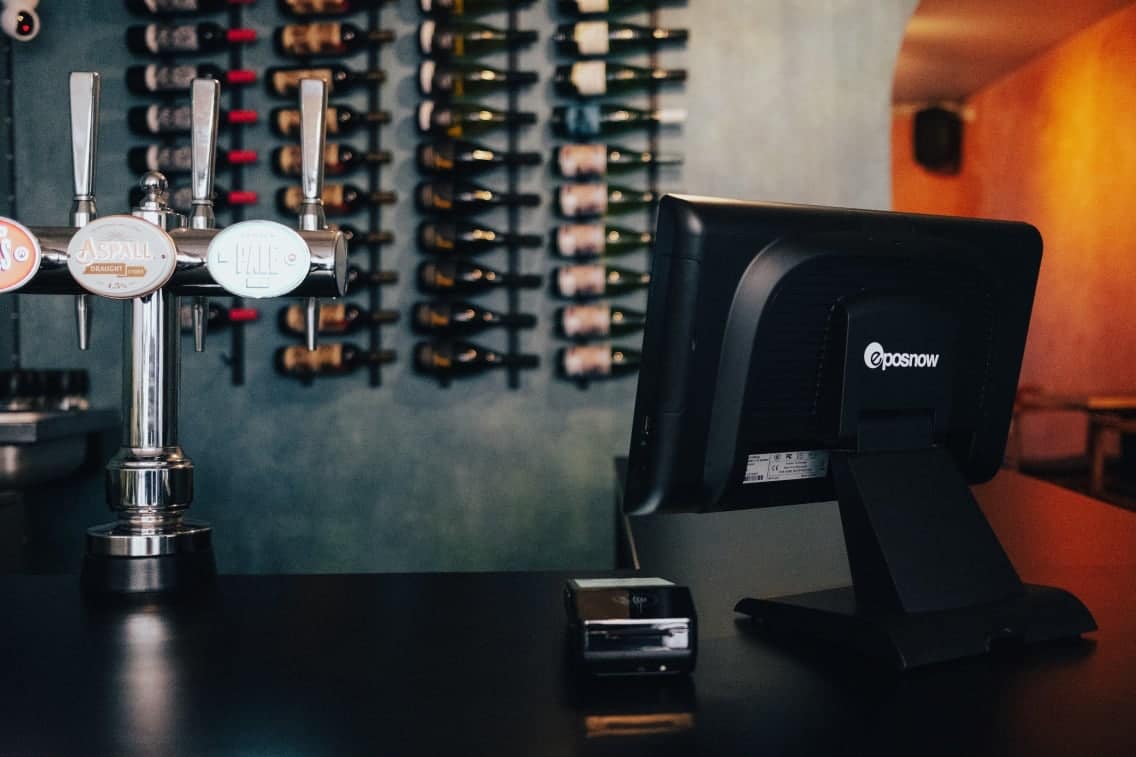 The POS equipment offered by the company carries the Epos Now brand Epos Now register hardware on a bar counter
